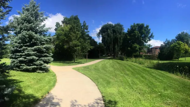 Image of a park in Vaughan with a paved path in the middle and trees along the left side of the path.