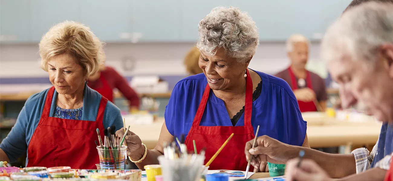 Older adults wearing red aprons and participating in a painting workshop