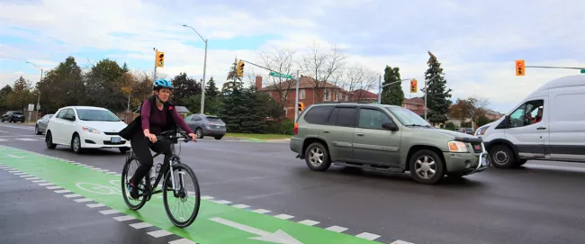 A cyclist riding in a designated bike-lane with traffic driving in the background.