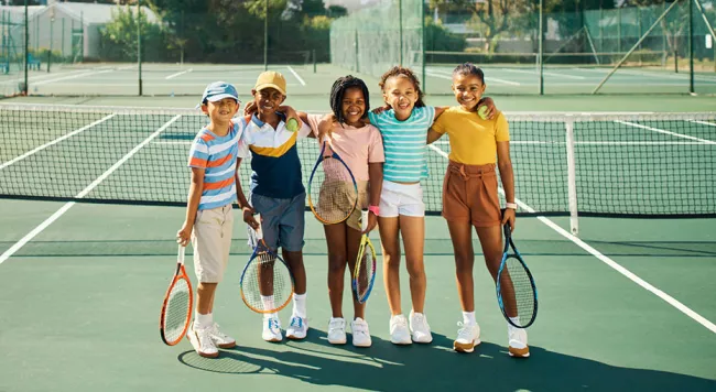 Kids holding tennis rackets on a tennis court