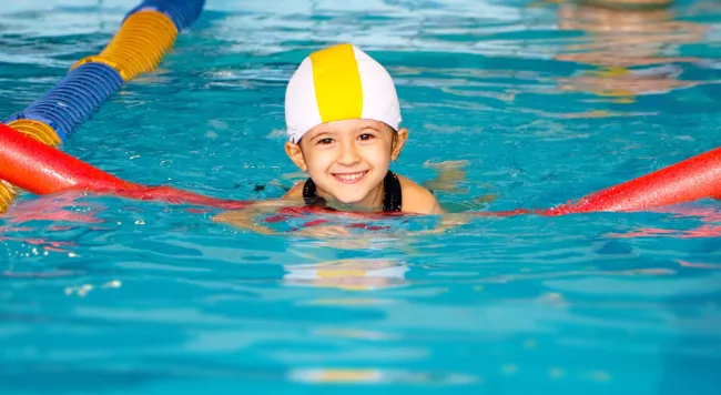 Child swimming in a pool with a red noodle 