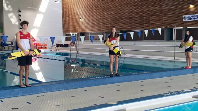 Three lifeguards standing by an indoor pool