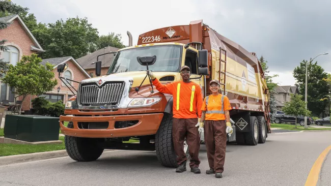 two waste collection workers beside their truck