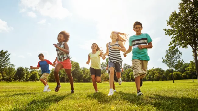 Five kids running in a field on a sunny day. 