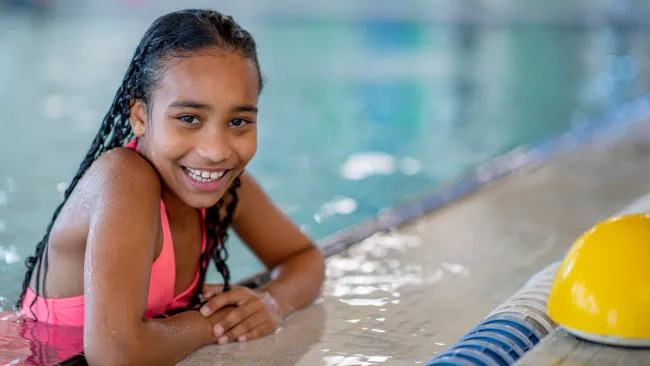 Young girl hanging on the side of a pool at a community centre.