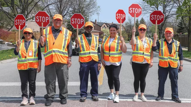 Six School Crossing Guards standing at a crosswalk holding up a stop sign