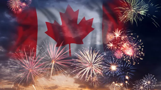 Fireworks going off in the sky with the Canada Flag in behind them. 