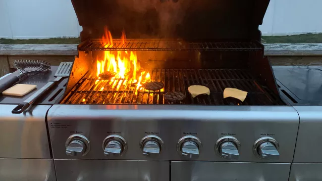 an outdoor barbecue with burgers on the grill. there are flames under some of them. 