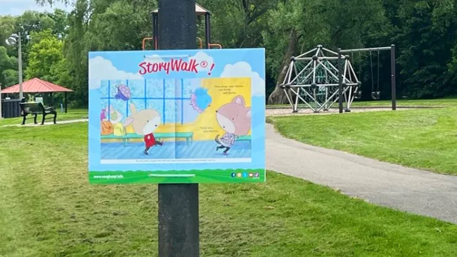 A StoryWalk board in along a path in a park. 