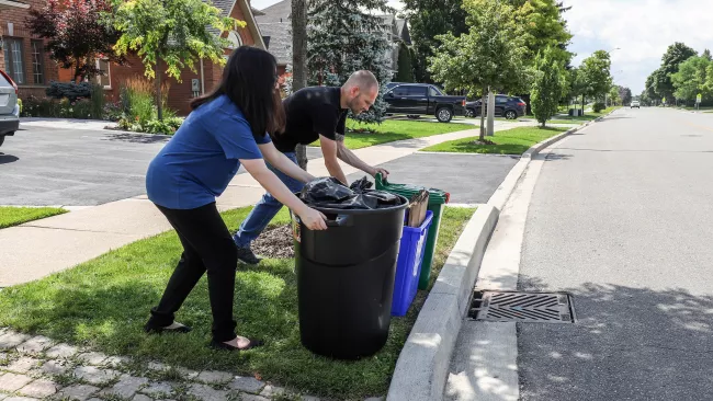 two people placing waste bins at the curb