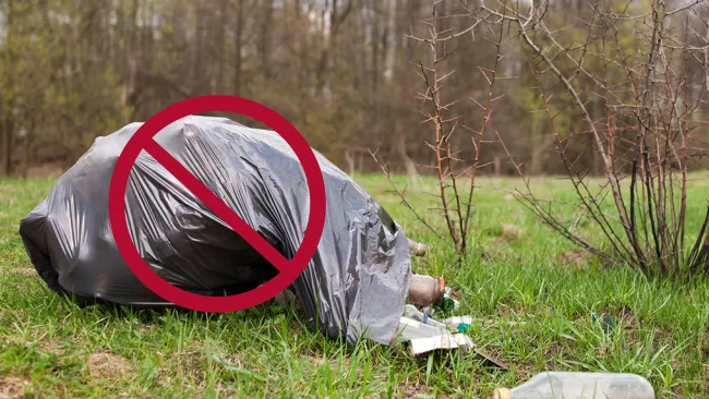 A garbage bag dumped on the side of the road with a stop symbol on top of it