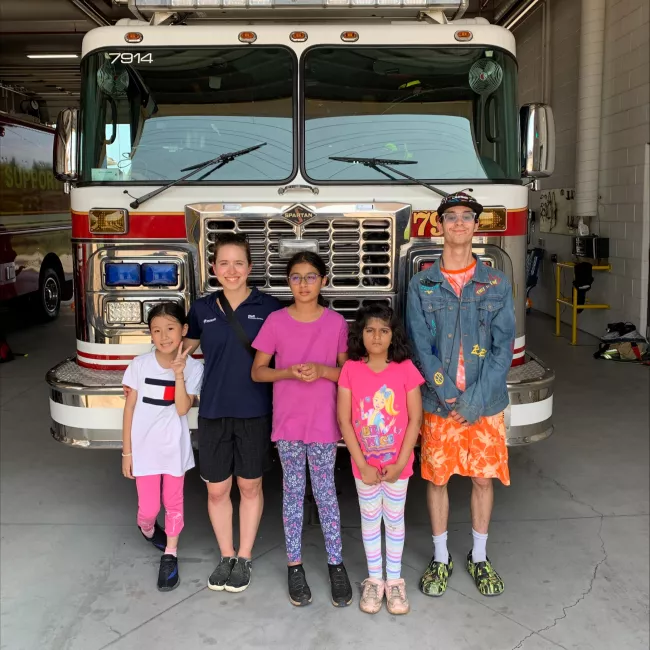 A camp counsellor and four campers posing in front of the front of a fire truck.