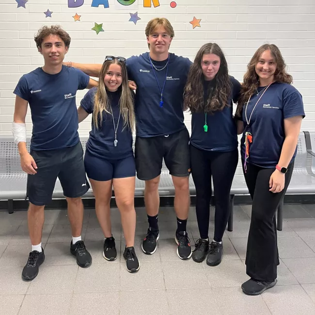 A group of five young Caucasian camp counsellors, two males and three females.