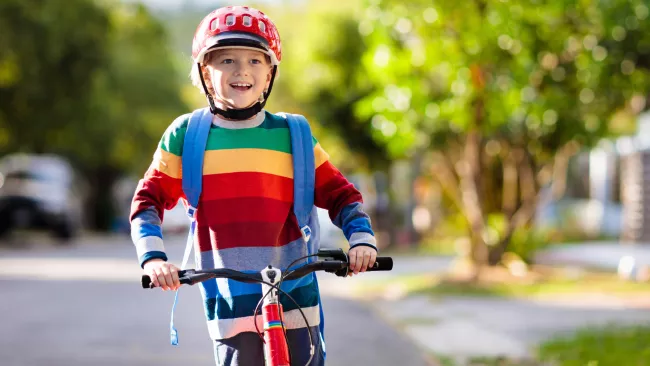 A kid in a striped sweater on a scooter with a helmet and backpack on .