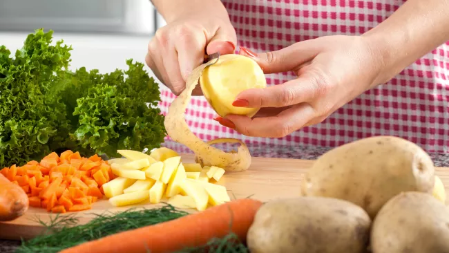 someone peeling a potato on a cutting board