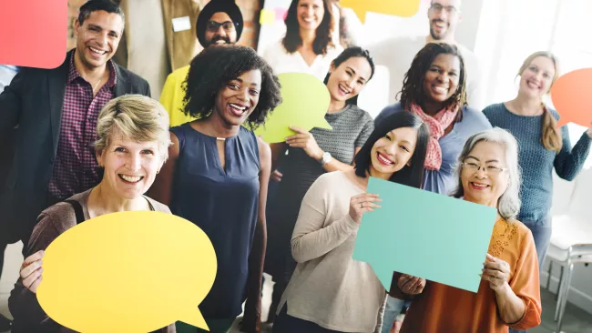 An image of a group of people standing in a room, smiling and holding speech bubble signs