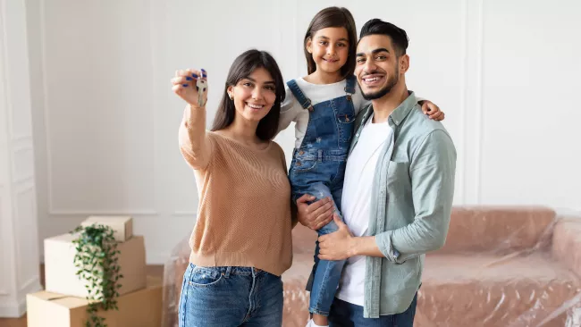 A young family standing in their new home holding the keys and smiling. 