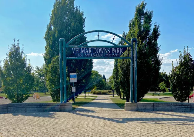 A green entrance gate to Velmar Downs Park with several trees behind it.