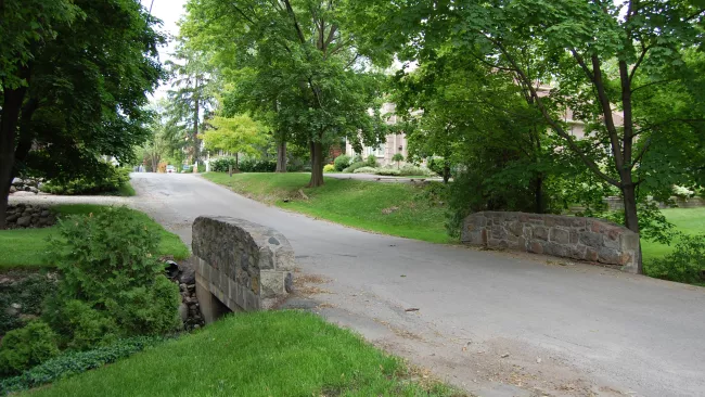 An image of a small bridge with stone sides and trees around it.