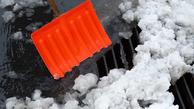 an orange shovel pushing snow off a catch basin