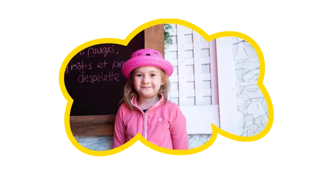 Girl wearing a pink outfit in front of a chalkboard that has French writing on it 