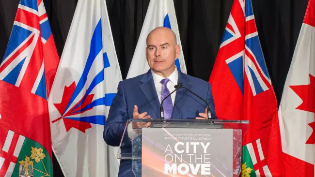 Mayor Del Duca speaking at a podium in front of Vaughan, Ontario and Canadian flags