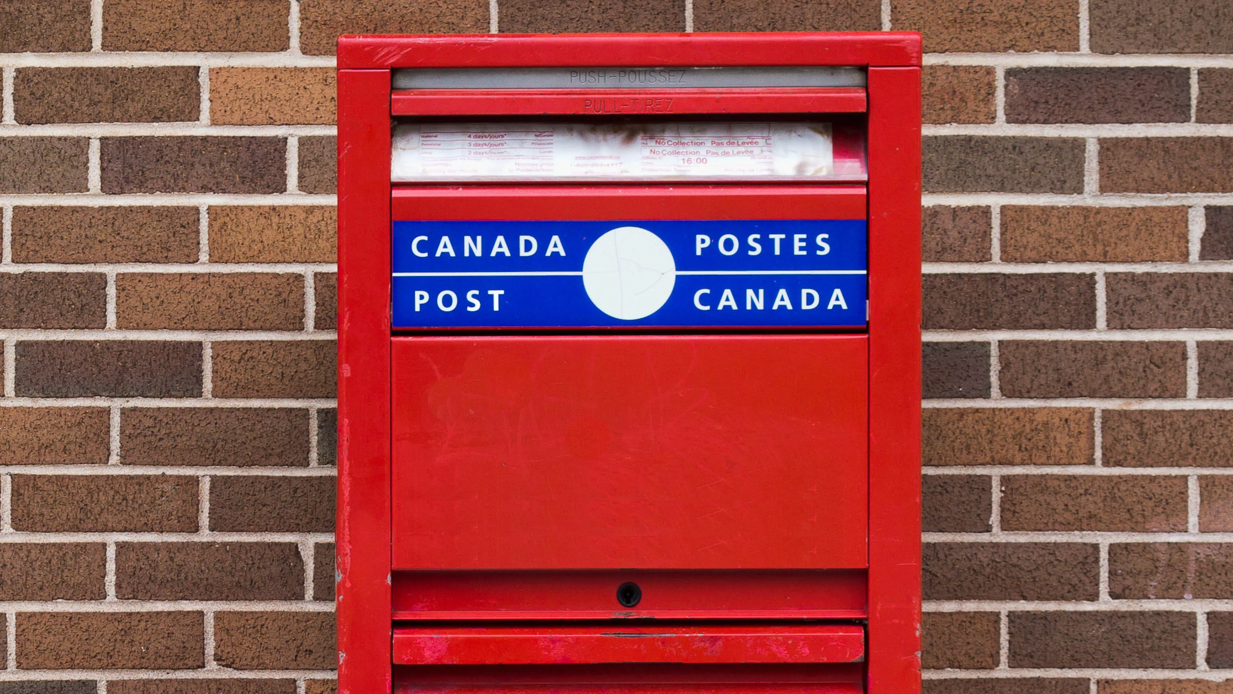 Canada Post mailbox against a brick wall. 