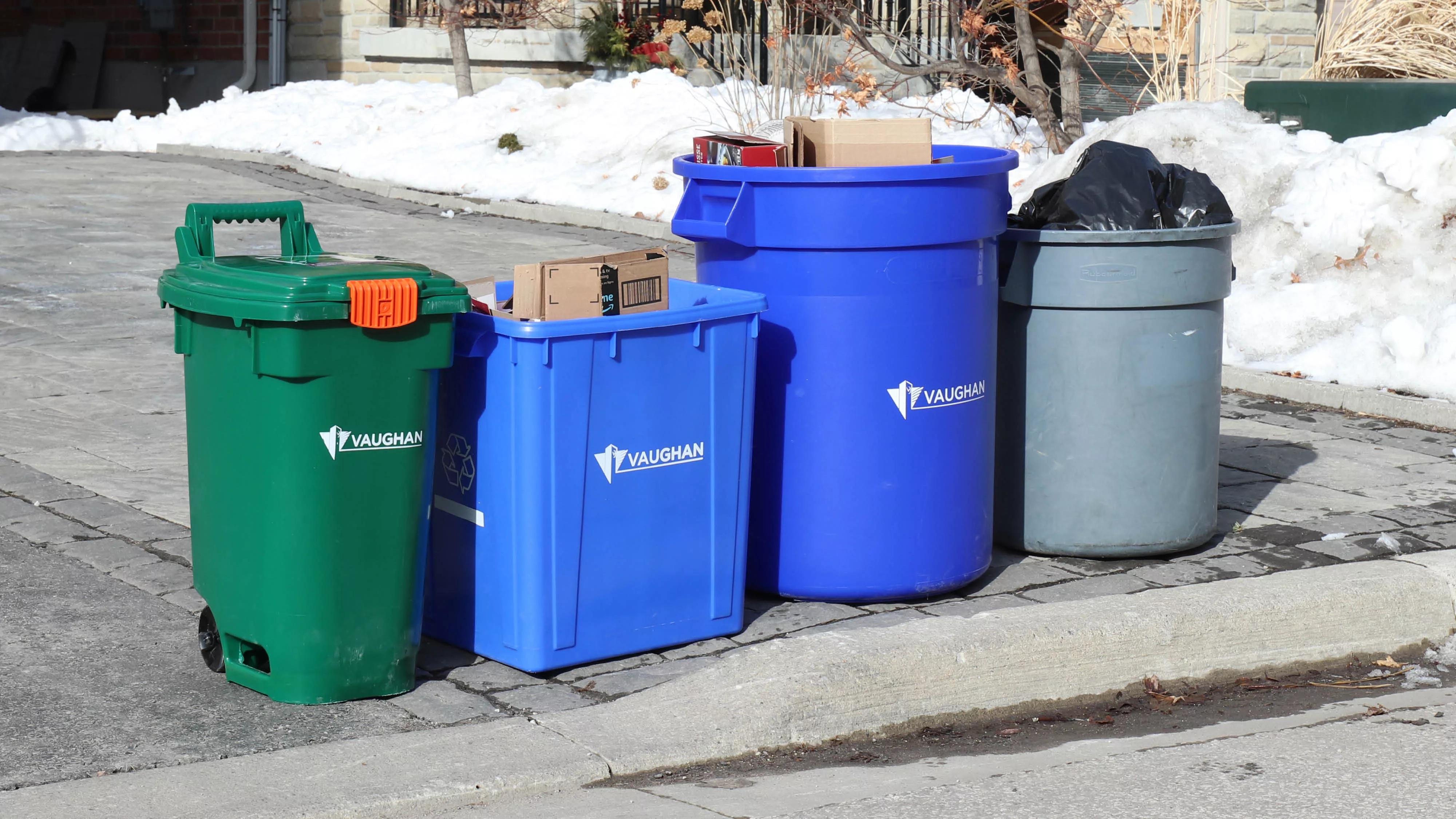 blue boxes, green bin and garbage at the end of a driveway