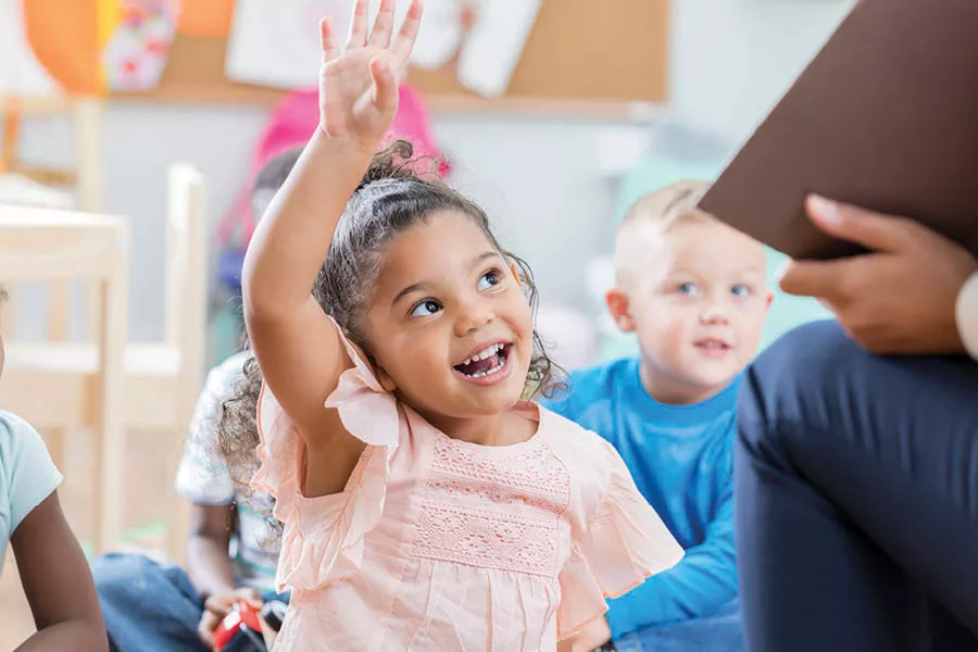 Little girl of mixed race, wearing a pink shirt smiling and raising her hand up