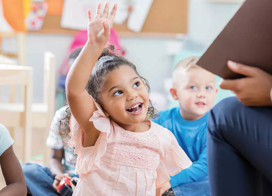 Little girl of mixed race, wearing a pink shirt smiling and raising her hand up 